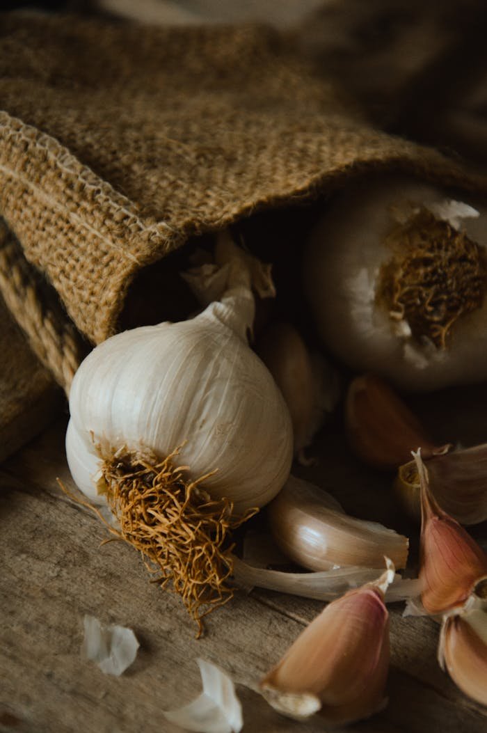 A sack of fresh garlic bulbs on a wooden surface with a rustic burlap texture.